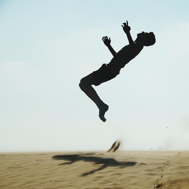 Silhouet van een volwassen man die op het zand op het strand springt tegen een heldere lucht