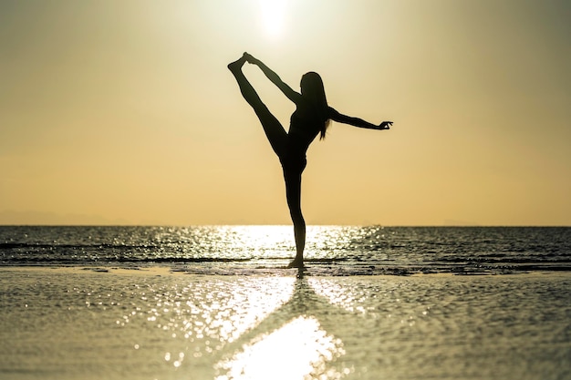 Silhouet van een vrouw die bij de yoga staat op het tropische strand tijdens zonsondergang Kaukasisch meisje dat yoga beoefent in de buurt van zeewater
