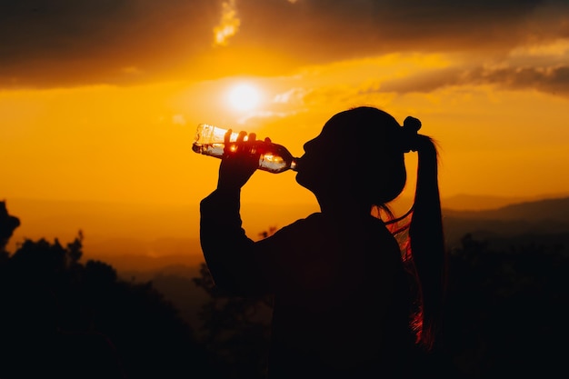 Silhouet van een vrouw die drinkwater drinkt in de zonsondergang