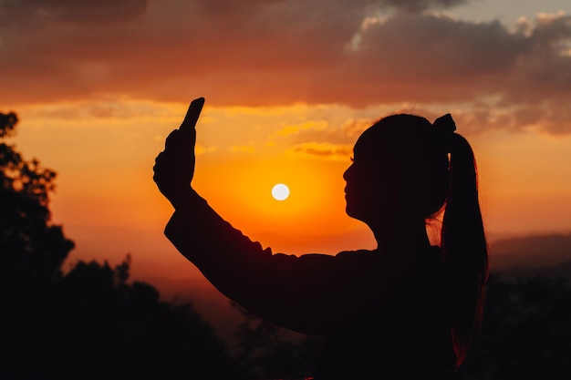 Silhouet van een vrouw die een foto neemt in het midden van een prachtige zonsondergang op de berg.