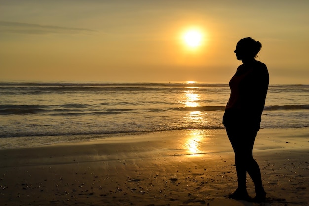 Silhouet van een vrouw die sensueel poseert aan de kust van een strand bij zonsondergang Het gouden uur