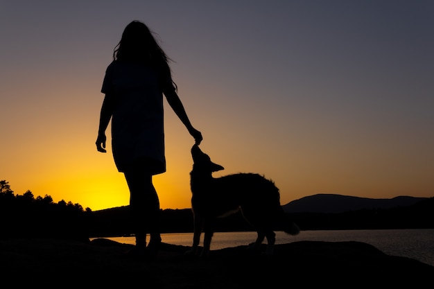 Foto silhouet van een vrouw die speelt met een hond bij zonsondergang voor een meer liefde voor dieren ruimte kopiëren