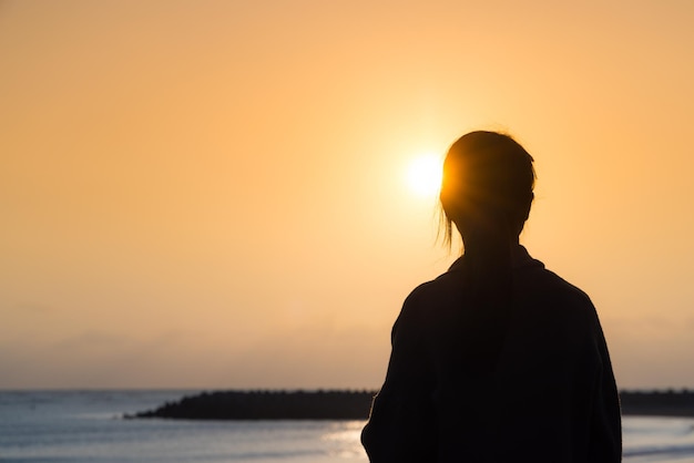 Silhouet van een vrouw die van de zonsondergang geniet op het strand.