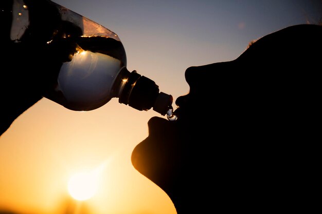 Silhouet van een vrouw die water drinkt bij zonsondergang