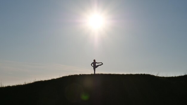 Silhouet van een vrouw die yoga-fitness doet in de natuur op een zonnige dag of zonsondergang Persoon die haar terug toont in een Utthita Hasta Padangusthasana Gezond vrouwelijk lichaam in sportkleding