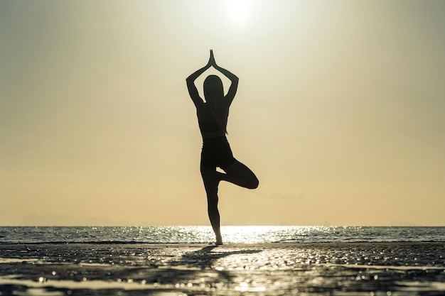 Silhouet van een vrouw die zich bij yoga poseert op het tropische strand tijdens zonsondergang Meisje dat yoga beoefent in de buurt van zeewater