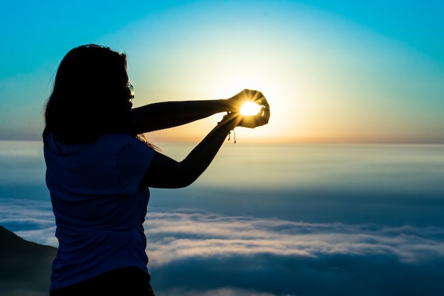 Silhouet van een vrouw die zonnebaadt met haar handen op de top van een berg