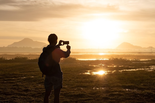 Silhouet van een vrouw met een smartphone die buiten foto's maakt tijdens zonsopgang of zonsondergang