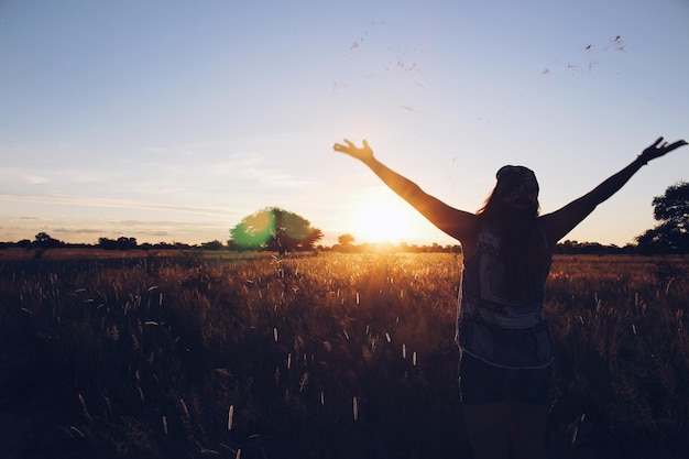 Silhouet van een vrouw met uitgestrekte armen die tijdens de zonsondergang op het veld staat