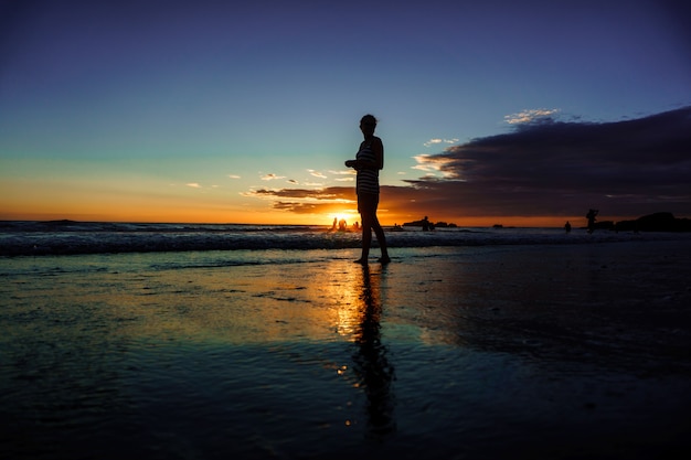 Silhouet van een vrouw op het strand bij zonsondergang, meisje dat over de zeekust loopt in het zomerzonlicht