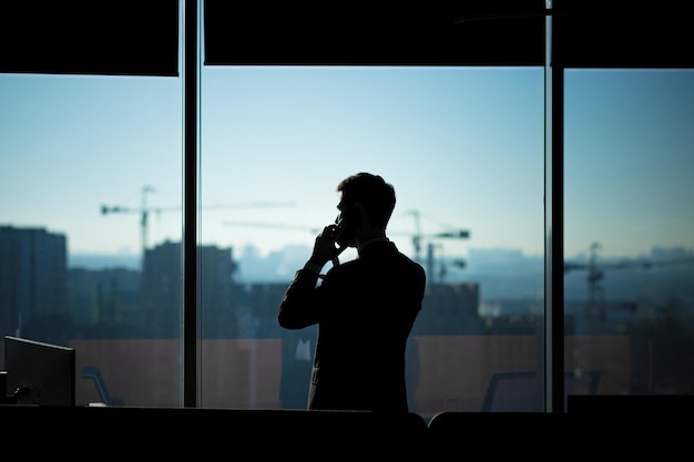 Silhouet van een zakenman man in een modern kantoor op de achtergrond van het raam een man praten aan de telefoon