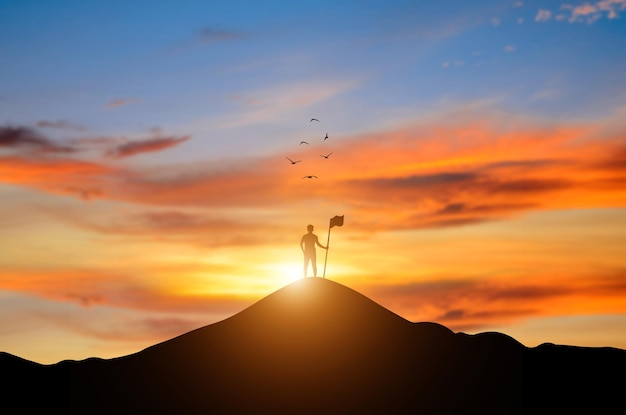 Foto silhouet van een zakenman met een vlag op de top van de berg bij zonsopgang en een vogel die over de lucht vliegt het is een symbool van leiderschap succesvolle prestatie met doel en objectief doel van het bedrijf