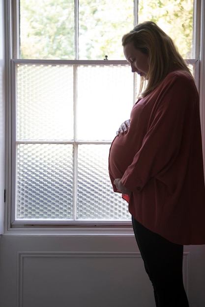 Silhouet van een zwangere vrouw die voor een raam staat