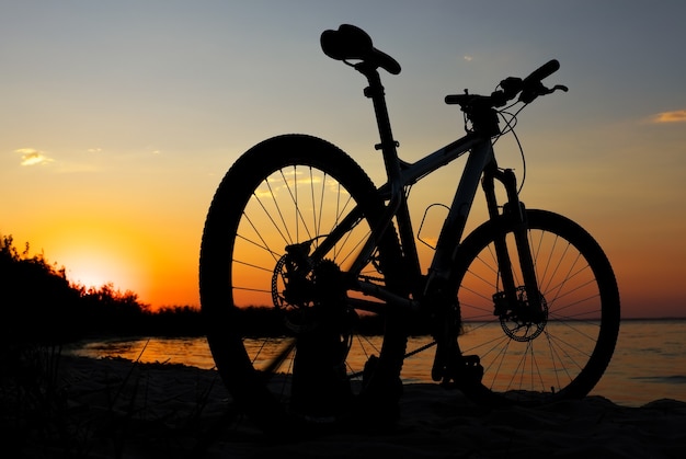 Silhouet van fiets op het strand tegen kleurrijke zonsondergang in de zee, gouden hemelachtergrond. Weerspiegeling van de zon in het water. Buitenshuis.