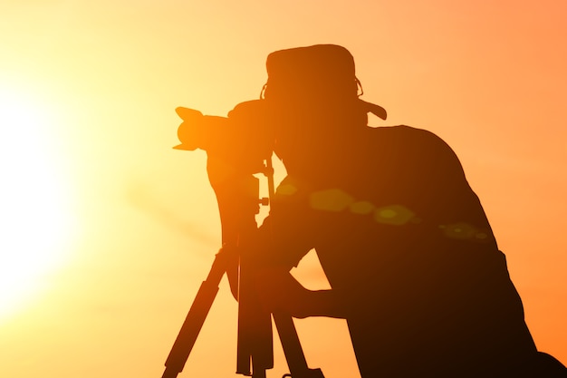 Silhouet van fotograaf met zijn uitrusting tijdens zonsondergang