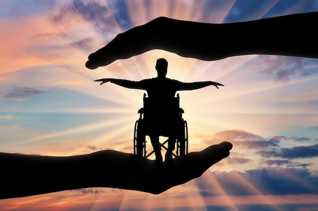 Silhouet van gelukkig gehandicapte man in rolstoel in handen van hulp. Het concept van bescherming en hulp aan mensen met een handicap