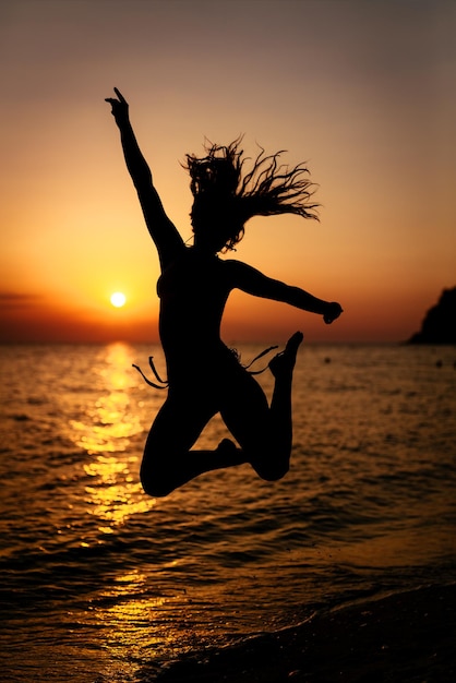 Silhouet van gelukkig meisje dat bij zonsondergang op het strand springt