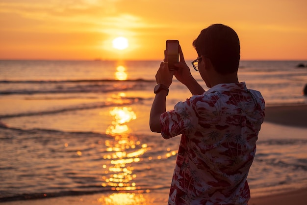 Silhouet van gelukkige jonge man die foto maakt door smartphoneTourist geniet van prachtige zonsondergang op het strand Reizen ontspannen vakantie zomer concept