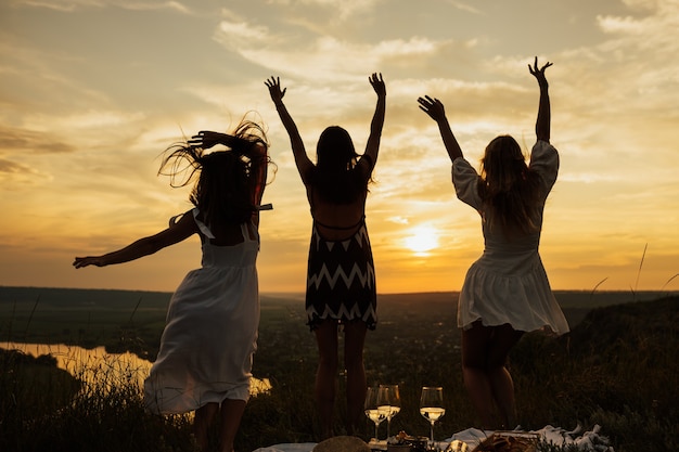 Silhouet van gelukkige meisjes met krullend haar stuiteren in zomerjurk met perfecte zonsondergang.