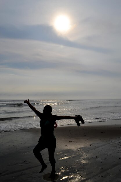 Silhouet van gelukkige vrouw die op de kust van een strand bij zonsondergang springt