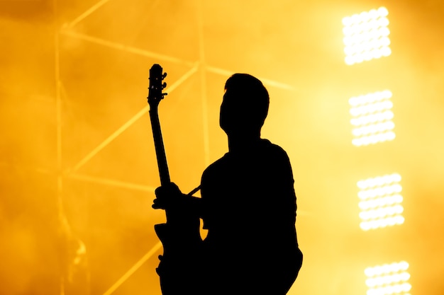 Silhouet van gitarist, gitarist presteren op concertpodium. oranje achtergrond, rook, concert schijnwerpers.