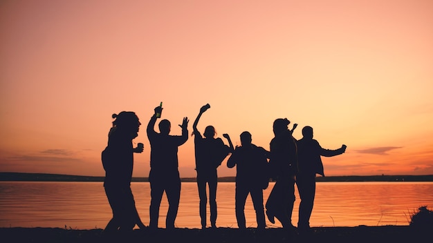 Silhouet van groep jonge dansende mensen hebben een feestje op het strand bij zonsondergang