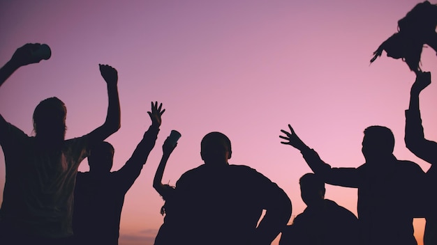 Silhouet van groep jonge dansende mensen hebben een feestje op het strand bij zonsondergang