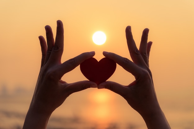 Foto silhouet van hand die rood hart houdt tijdens zonsondergangachtergrond.