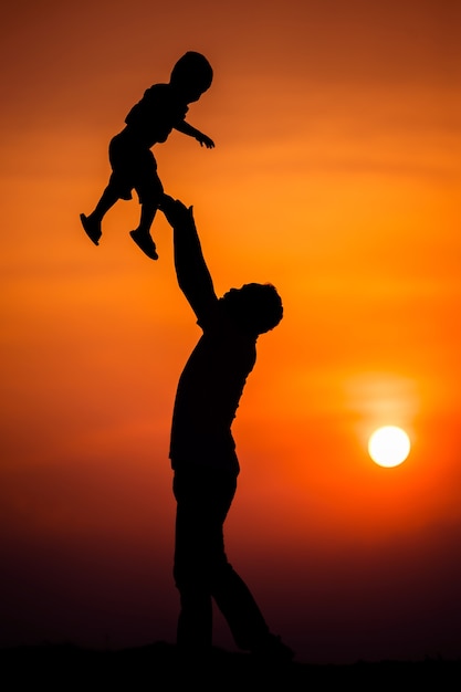 Silhouet van het gezin dat de vader vrolijk met de jongen speelt met de avondrood