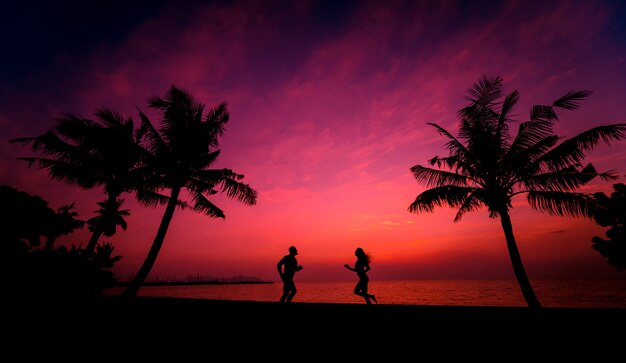 Silhouet van het paar op tropisch strand tijdens zonsondergang op de achtergrond