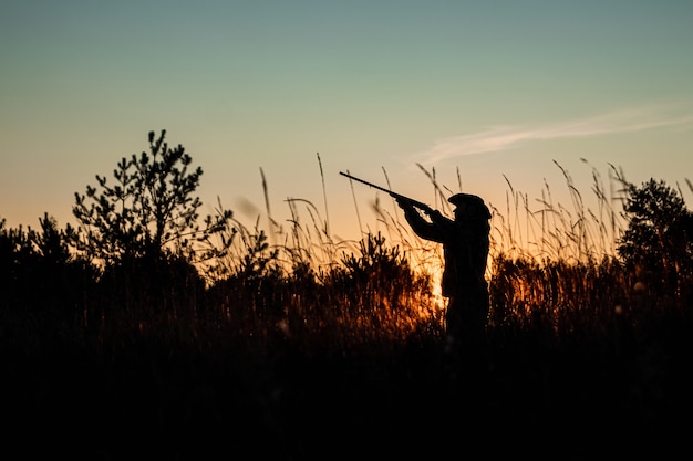 Silhouet van Hunter in een cowboyhoed met een pistool in zijn handen op een prachtige zonsondergang