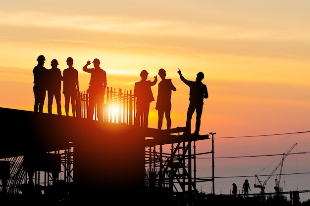 Silhouet van ingenieur en arbeidersteam op bouwplaats, bouwplaats in de industriële sector bij zonsondergang in de avondtijd