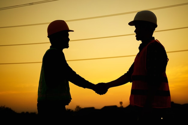 Silhouet van ingenieur en voorman werknemer handen schudden op bouwplaats tijdens zonsondergang