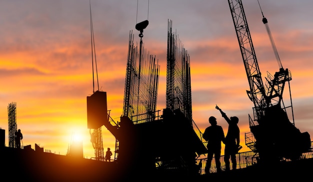 Silhouet van ingenieur en werknemer die project controleren op de bouwplaats op de achtergrond van de bouwplaats bij zonsondergang in de avondtijd