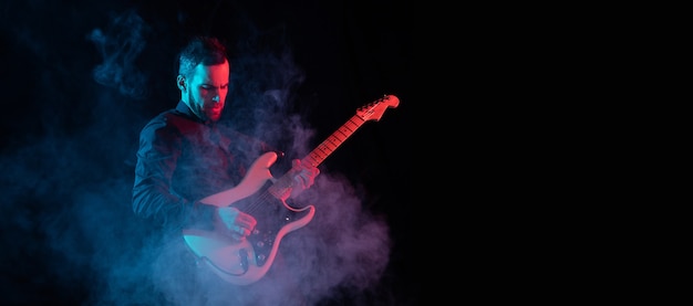 Silhouet van jonge blanke mannelijke gitarist geïsoleerd op blauw-roze gradiënt studio achtergrond in neon