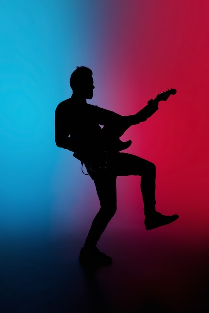 Silhouet van jonge blanke mannelijke gitarist geïsoleerd op blauw-roze gradiëntstudio in neonlicht