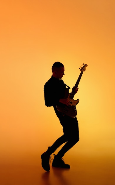 Silhouet van jonge blanke mannelijke gitarist geïsoleerd op blauwroze gradiëntstudio in neonlicht