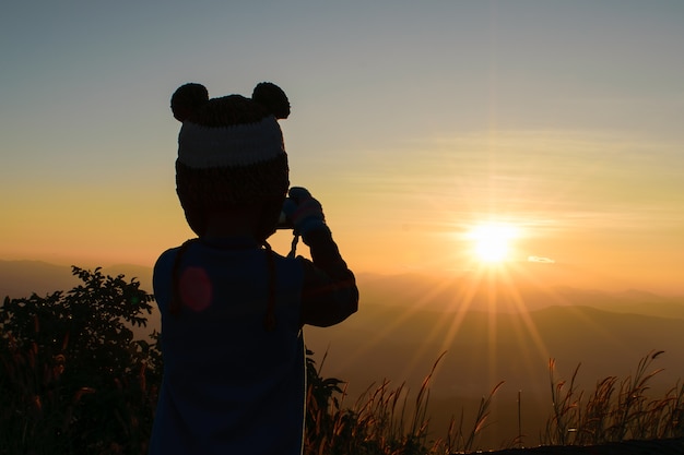 Silhouet van jonge fotograaf met zonsopgang op de berg.