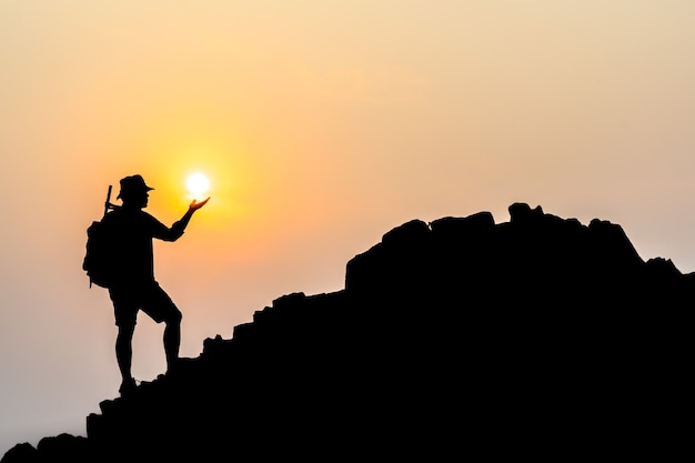 Silhouet van jonge mannelijke toeristen Sta en kijk met je rugzak naar de zonsondergang op de top van de berg.