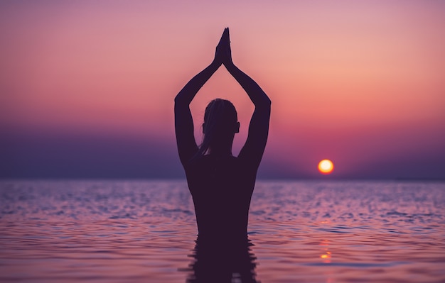 silhouet van jonge vrouw die yoga beoefent op het strand bij zonsopgang