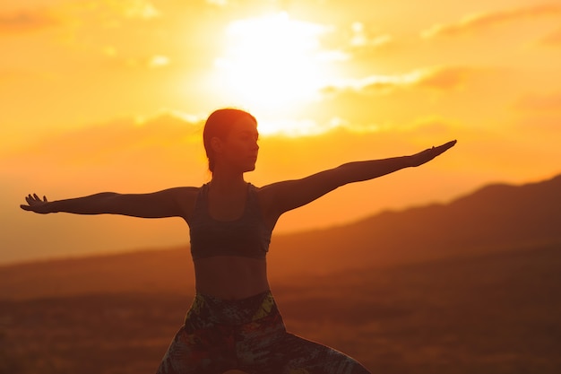 Silhouet van jonge vrouw het beoefenen van yoga bij zonsondergang