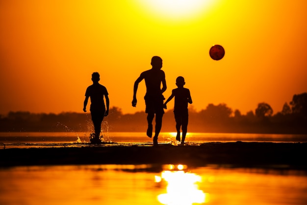 Silhouet van kinderen voetballen op het strand