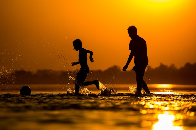 Silhouet van kinderen voetballen op het strand