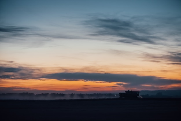 Silhouet van maaimachinemachine om tarwe op zonsondergang te oogsten.