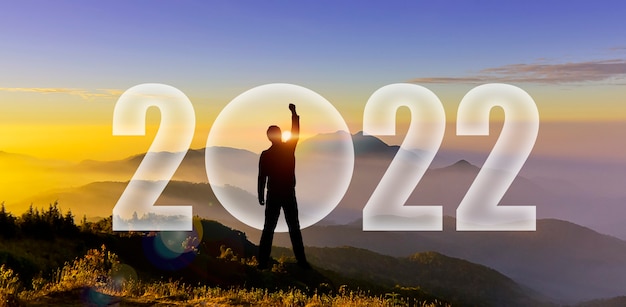 Silhouet van man handen omhoog om 2022 op bergheuvel uit te dagen. Gelukkig nieuwjaar 2022. Man silhouet bij zonsondergang, zonsopgang hand opsteken om 2022 te vechten op de berg show verandering, opstarten, doel, leider concept