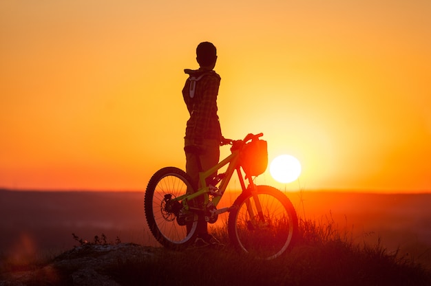 Silhouet van man met fiets op de top van de berg op zonsondergang