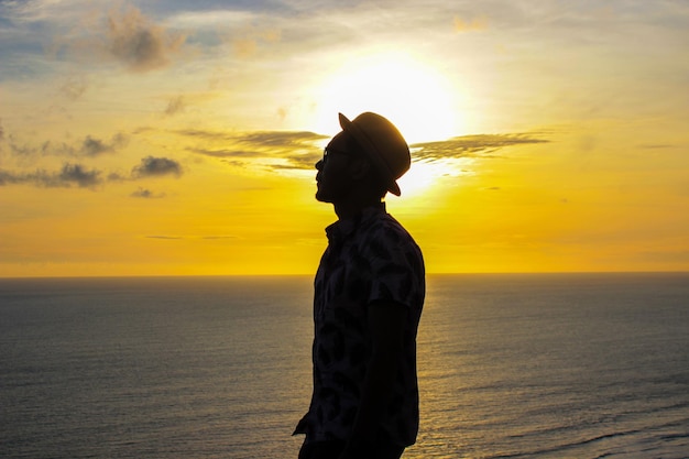 Silhouet van man met hoed tegen de achtergrond van de ondergaande zon in de oceaan