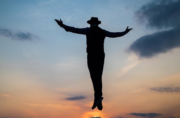 Silhouet van man zweven in zonsopgang hemel met opgeheven handen, vrijheid.