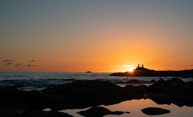 Silhouet van mannen die vissen bij zonsondergang