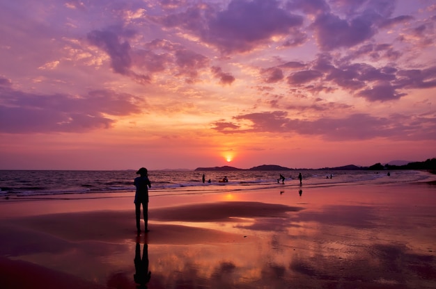 Silhouet van mensen die binnen aan het overzees met dramatische zonsonderganghemel spelen